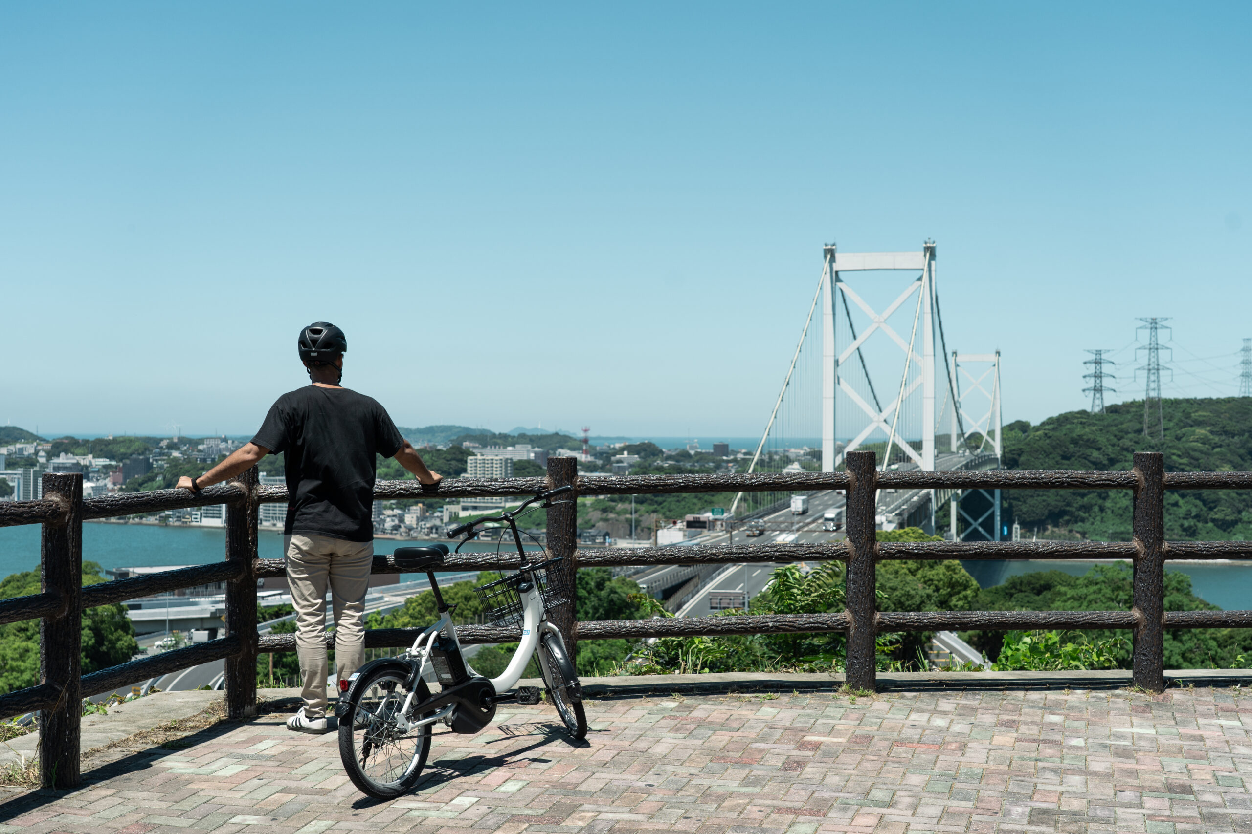 Cyclist standing with a bicycle at Mekari Park Second Observation Deck, viewing the Kanmon Bridge