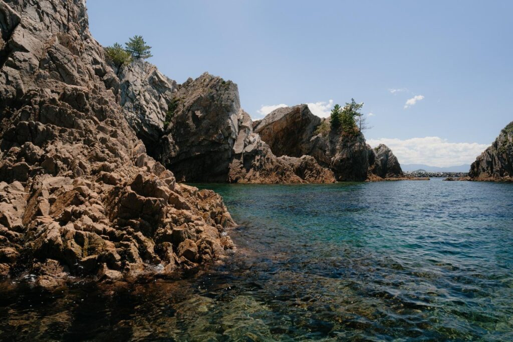 Translucent blue water laps the rocky shore of the Uradome Coast, as seen from the Uradome Coast Island Cruise